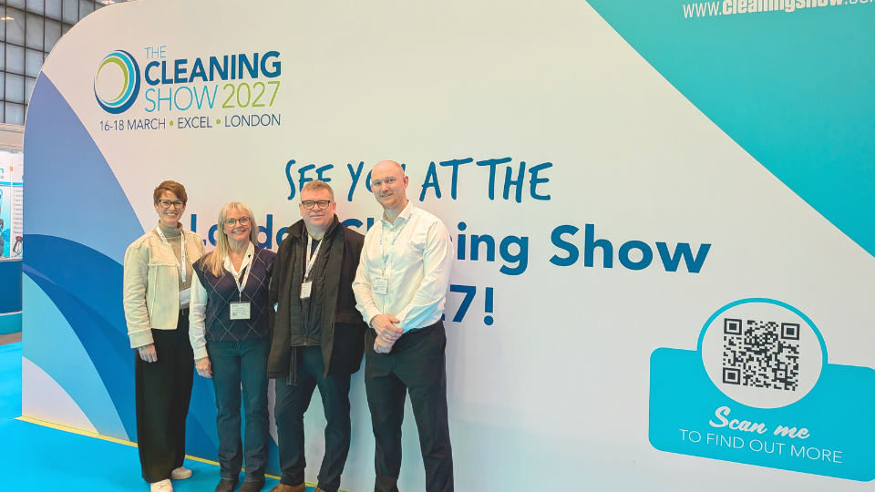 Four HW Facilities staff standing in front of The Cleaning Show banner