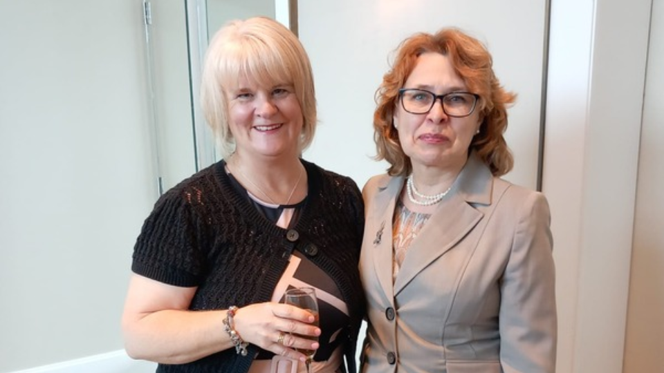 Emma (L) and Irina (R) standing together smiling at the camera
