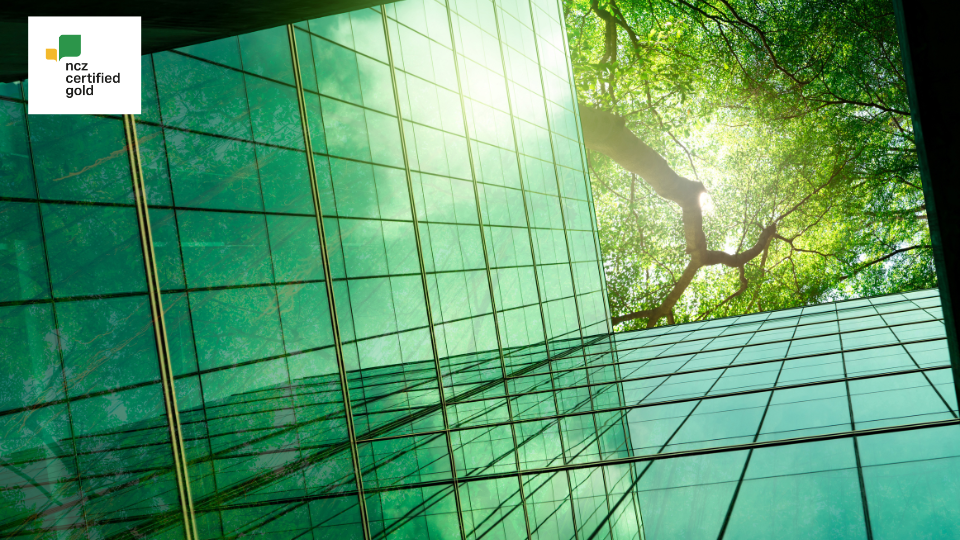 NCZ Certified Gold logo against glass building, healthy tree and sunlight